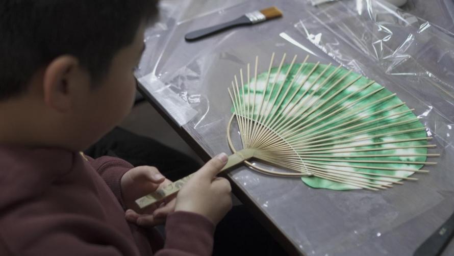 竹の骨組みに和紙を貼る「うちわ作り体験」をしている子供の手元